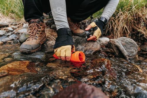 Preview: Hiker fills water bottle with fresh stream water during expedition in woods