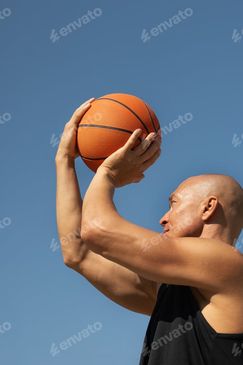Preview: Sporty man tries to throw ball into basketball hoop on sports court at courtyard. Game moment.