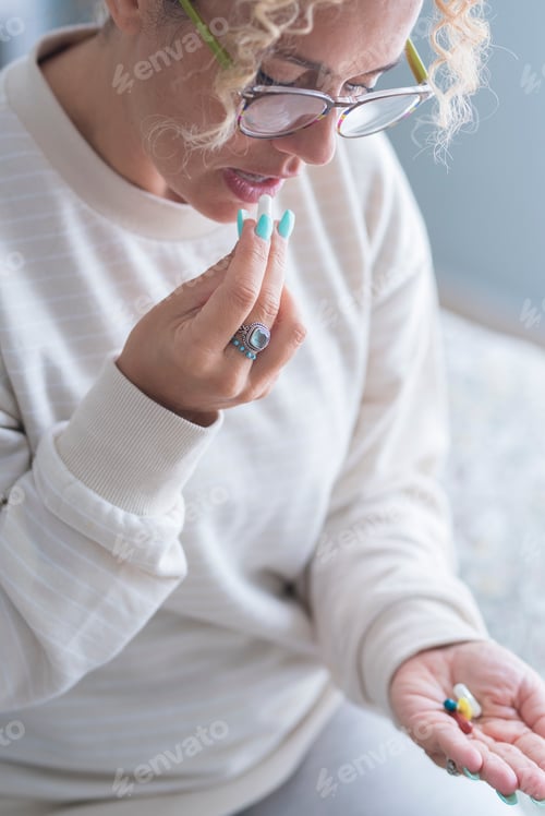Preview: Adult woman middle age taking pills medicine at home sitting on bed alone - disease and healthy