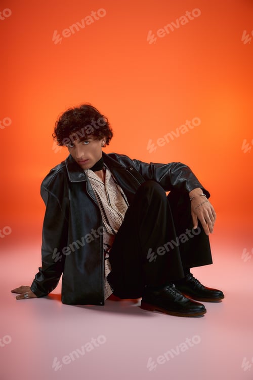 Preview: Handsome stylish man posing elegantly against a vibrant orange backdrop in a fashion focused setting