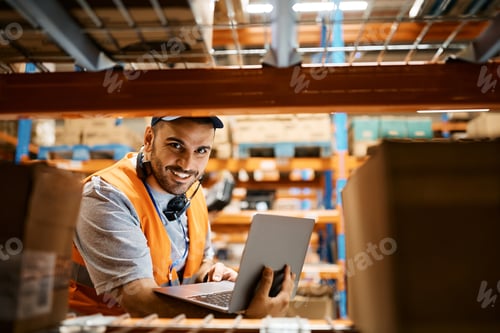 Preview: Happy warehouse worker using laptop and looking at camera.