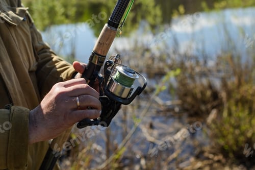Preview: Outdoors close-up of a man's hand spinning a fishing rod reel, pulling the caught fish, copy space.