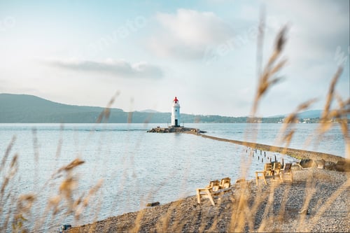 Preview: White lighthouse on the seashore. Seascape with spikelets in bokeh in the foreground.