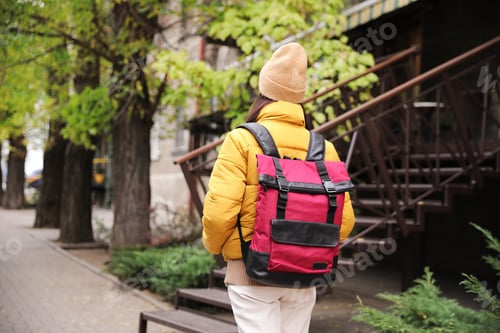 Preview: Female tourist with travel backpack on city street, back view. Urban trip