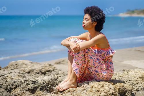 Preview: African American tourist sitting on stone and breathing fresh sea air