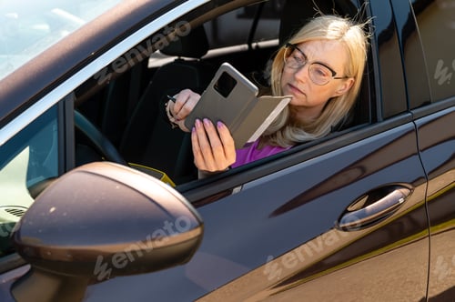 Preview: a middle-aged blonde woman in glasses with a smartphone looks through an open car window