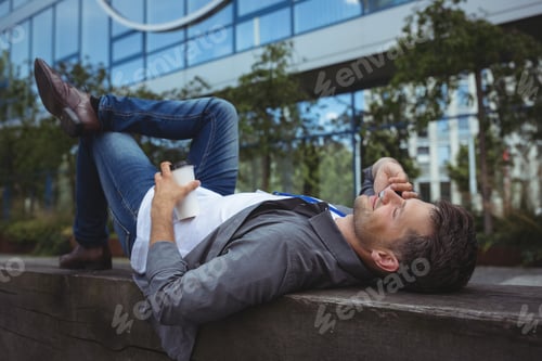 Preview: Handsome Business Executive Lying On Wood While Talking On Mobile Phone