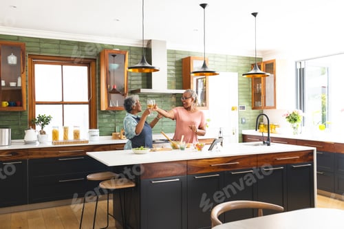 Preview: Senior African American woman and senior biracial woman toast in a bright kitchen