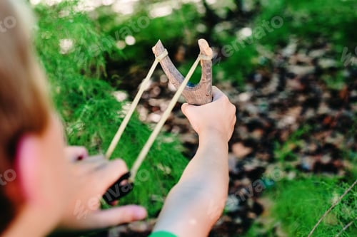 Preview: Child playing with his slingshot in a park having fun in freedom.