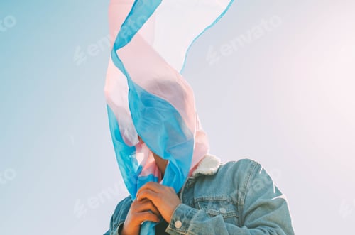 Preview: Unrecognizable man covering his face with the trans flag against the clear sky