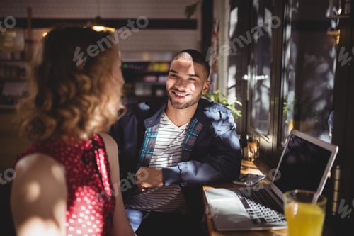 Preview: Smiling young man talking with female friend sitting at coffee shop