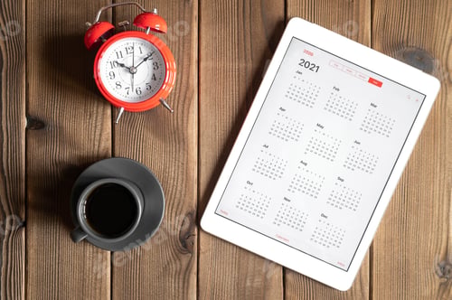 Preview: tablet with calendar for 2021, a cup of coffee and a red alarm clock on a wooden background flat lay