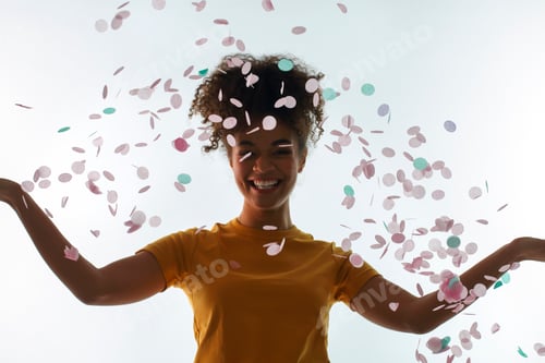 Preview: Happy African ethnicity young woman throwing colored confetti up into air