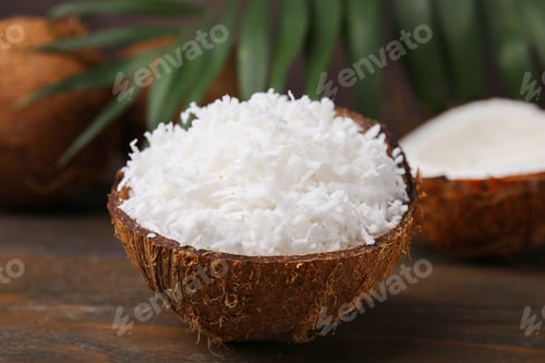 Preview: Coconut flakes in nut shell on wooden table, closeup