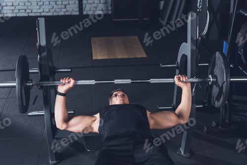 Preview: young athletic man lifting barbell alone in gym