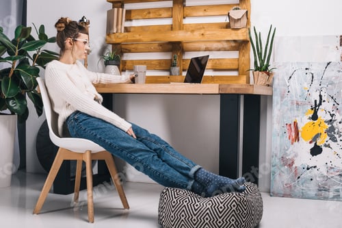 Preview: girl holding cup of tea and looking at laptop in office