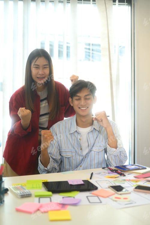 Preview: Two young professionals celebrating their achievement in a creative workspace