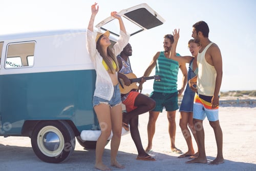 Preview: Side view of happy group of diverse friends having fun together near camper van at beach