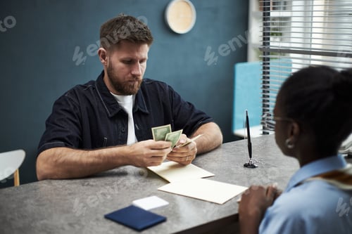Preview: Caucasian Young Man Counting Cash While Standing at Bank Office Desk