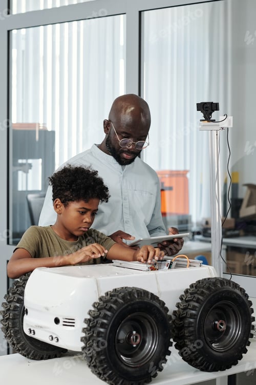 Preview: Clever schoolboy connecting cables of crawler while teacher giving instructions