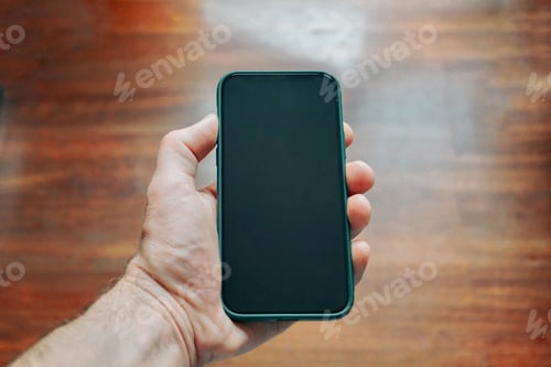 Preview: Closeup of a hand holding a smartphone with black screen on blurred wooden background
