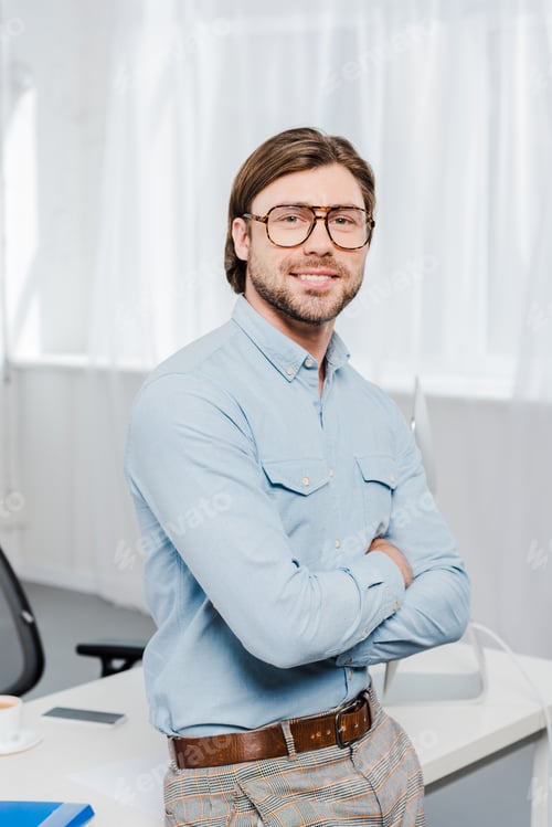Preview: handsome young businessman with crossed arms looking at camera at modern office