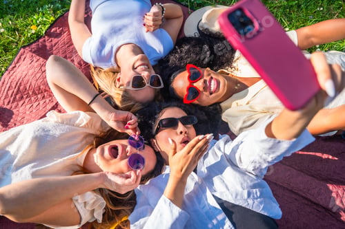 Preview: Four young women taking a selfie lying on a blanket in a park