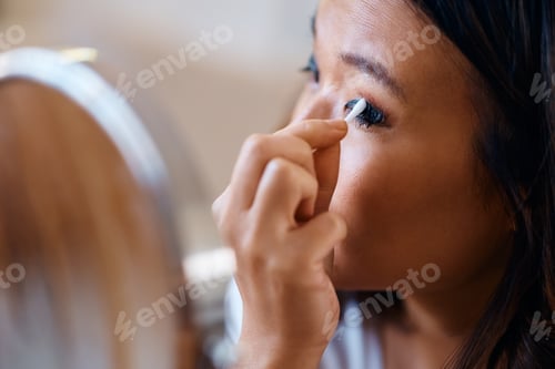 Preview: Close up of Asian woman removing makeup form her eyes at home.