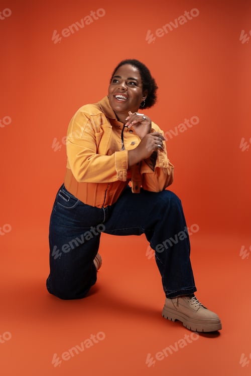 Preview: Stylish plus size woman in trendy autumn outfit poses confidently in a vibrant studio