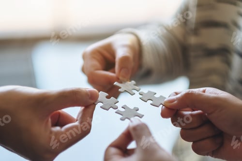 Preview: Closeup image of many people holding and putting a piece of white jigsaw puzzle together