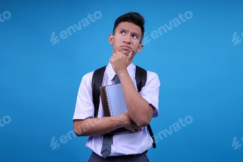 Preview: Thoughtfully High School Student Guy Thinking With Hand On Chin Standing On Blue Background