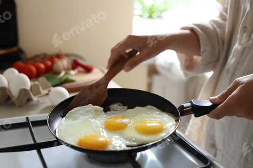 Preview: Woman cooking tasty eggs on frying pan in kitchen, closeup