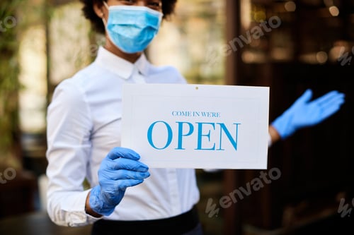 Preview: Close-up of waitress holding open sign while wearing protective face mask and gloves.