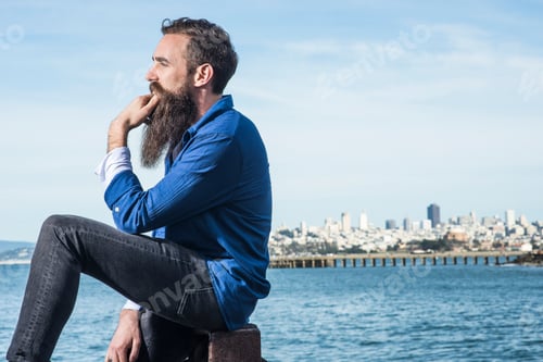 Preview: Man pondering by the sea with city skyline in the background