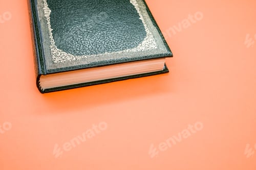 Preview: Top view closeup of an ancient book with a dark green cover isolated on an orange background