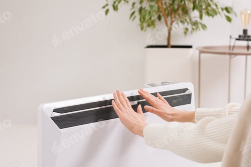 Preview: Unwell woman renter in blanket sit in cold living room hand on old radiator