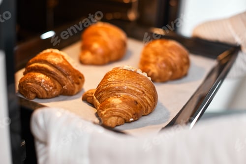Preview: female baker taking tray with fresh croissants from oven