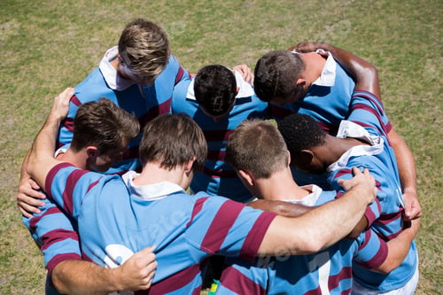 Preview: High angle view of rugby team making huddle while standing at playing field