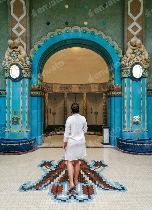 Preview: Rear view young woman wearing white satin bathrobe, standing on mosaic tiles in amazing indoor spa