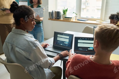 Preview: Teenage Girl and Caucasian Teenage Boy Collaborating on Laptops in Classroom