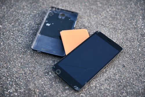 Preview: Damaged smartphone with broken touch screen on asphalt
