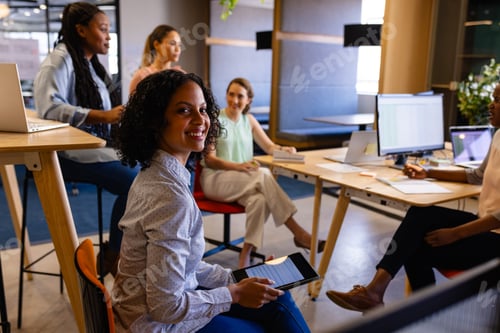 Preview: Portrait of happy biracial casual businesswomen holding tablet in office