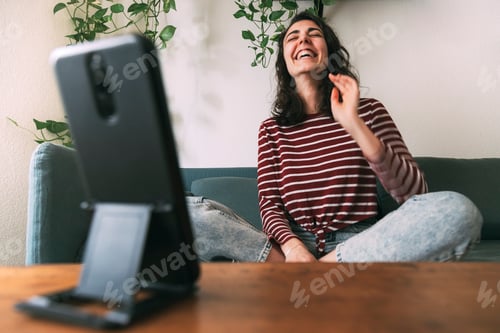 Preview: Girl laughs looking at phone sitting on the sofa at home. Selective focus on girl. At home concept
