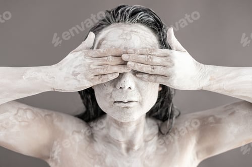 Preview: Art portrait of asian woman covered in clay isolated over grey background. Woman face like cracked p