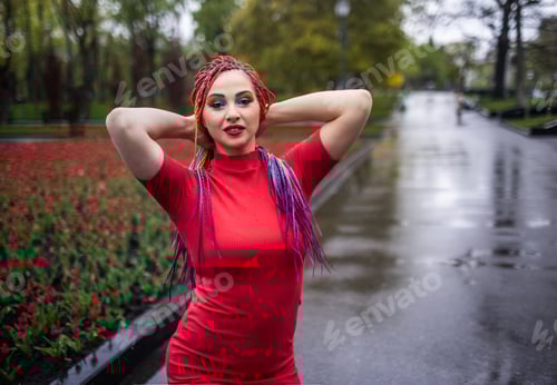 Preview: Cute girl with multi-colored African braids and bright expressive makeup in a tight red dress is