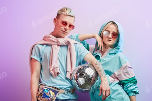 Preview: Young fashionable couple of dancers posing with disco ball on violet background