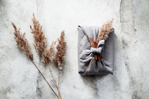 Preview: Top view of wrapped gift by linen fabric in furoshiki eco style with Autumn decor.