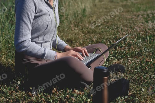 Preview: Young girl student sitting on a grass in a park using laptop computer