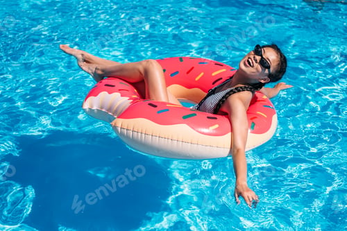 Preview: Young asian woman floating on inflatable donut in swimming pool