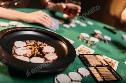 Preview: cropped image of girl playing poker at table in casino, roulette and cigars on foreground
